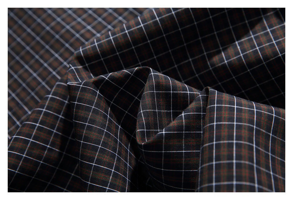 Close-up of dark plaid fabric gathered into folds, showing a fine white and rust-colored windowpane pattern.