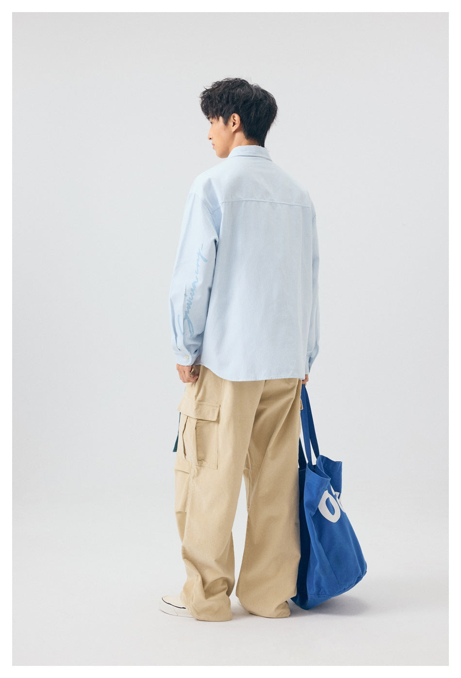 Rear view of a model wearing a pale blue shirt with sleeve lettering and beige cargo pants.