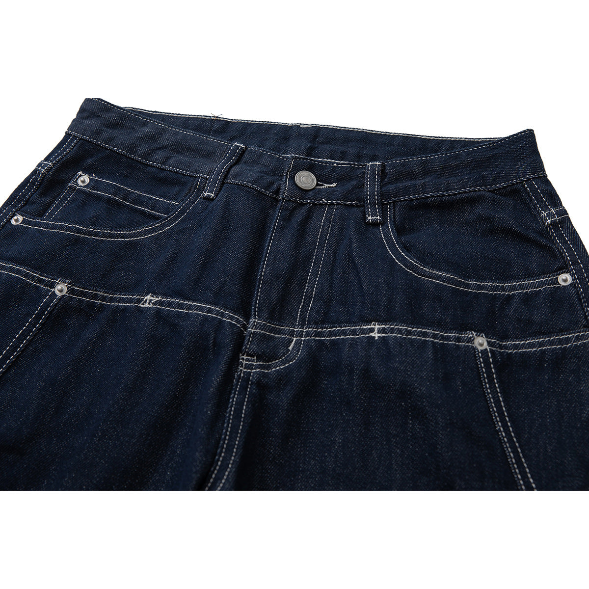 Close-up of dark indigo jeans showing the front waistband, button, riveted pockets and contrast stitching.