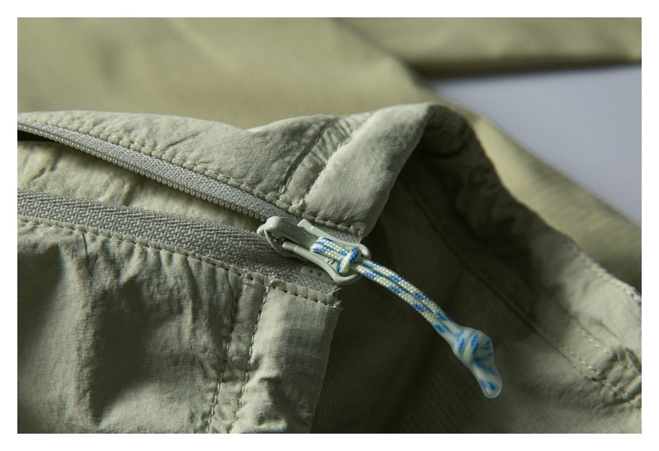 Close-up of a pale sage garment zipper with a blue-and-white cord pull.