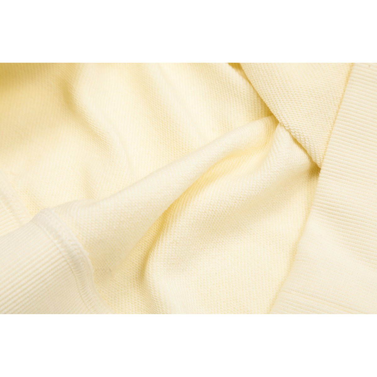Extreme close-up of cream sweatshirt fabric and a ribbed edge, showing the knit texture.