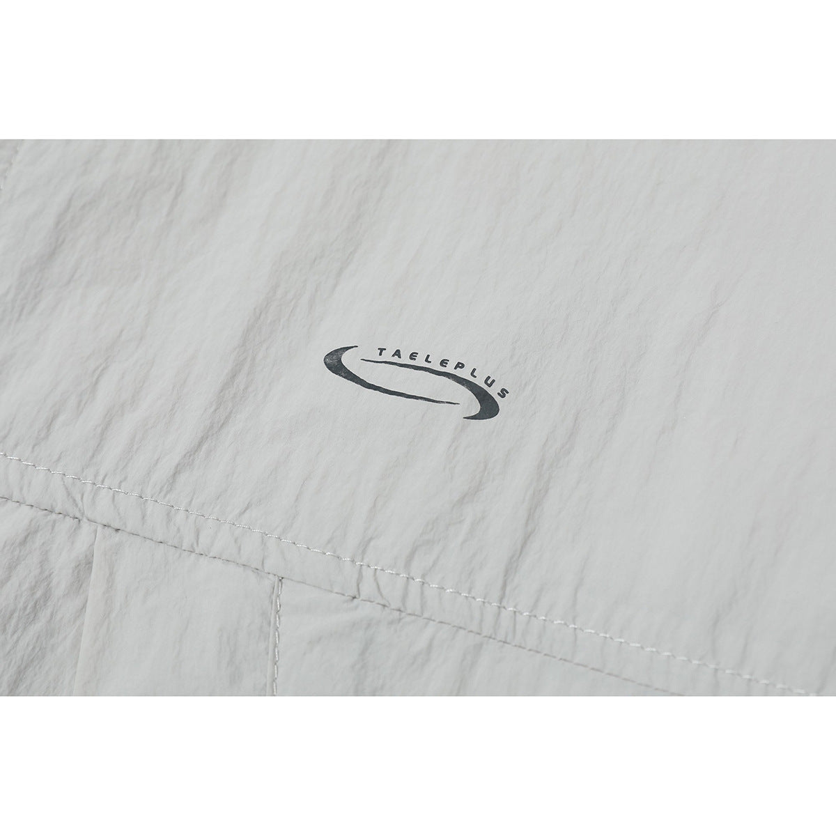 Close-up of a small black TAGLEPLUS logo printed on light gray jacket fabric.