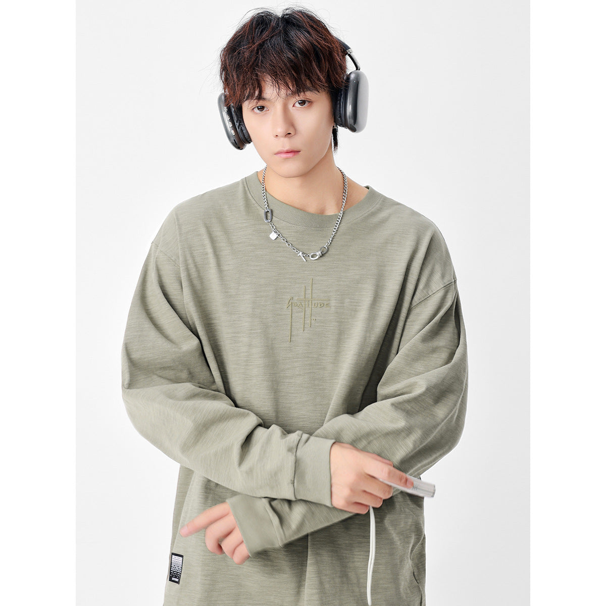 Model wearing a muted sage oversized long-sleeve shirt with a small tonal chest graphic.