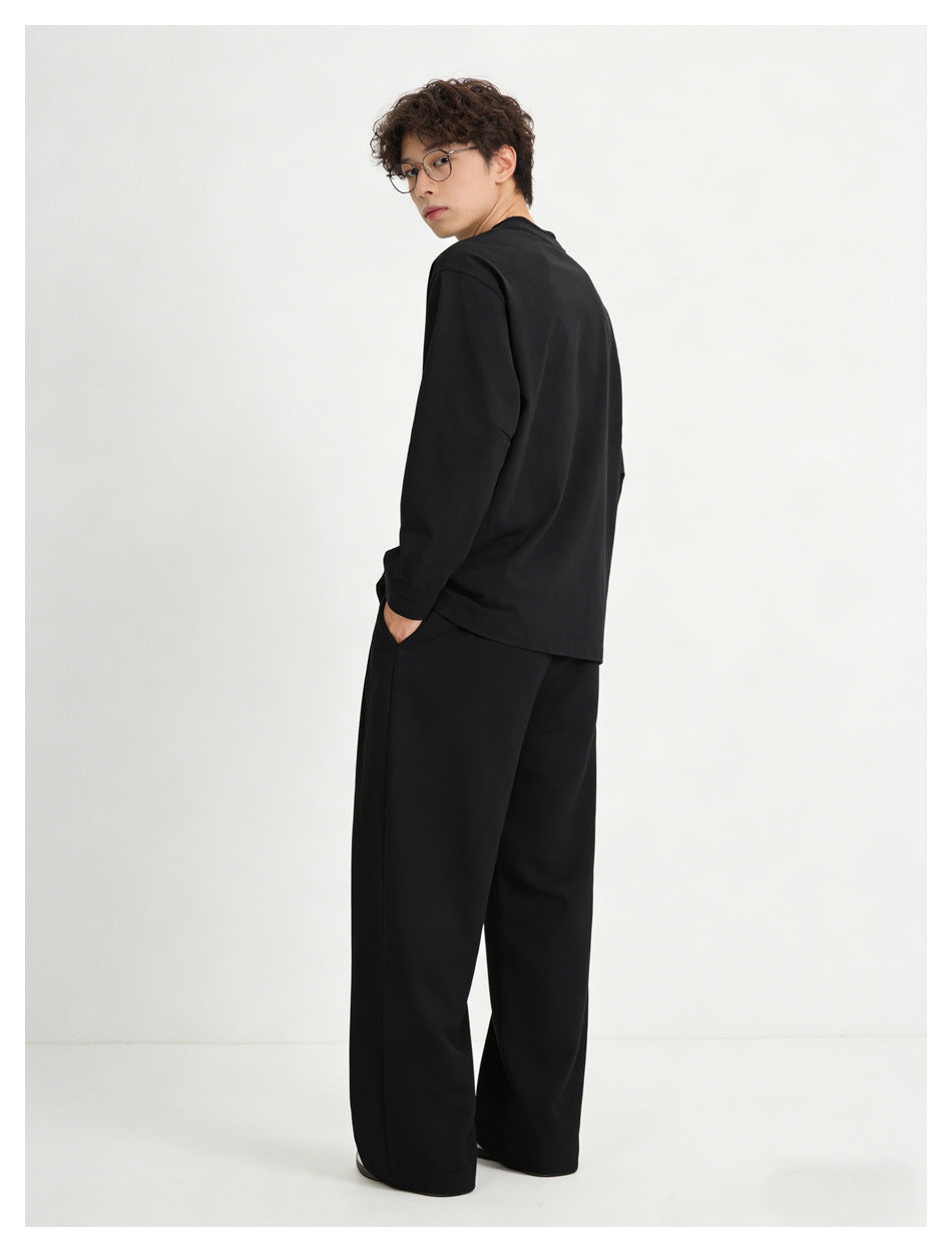 Model showing the back of a plain black crewneck sweatshirt with black wide-leg trousers, glancing over his shoulder.