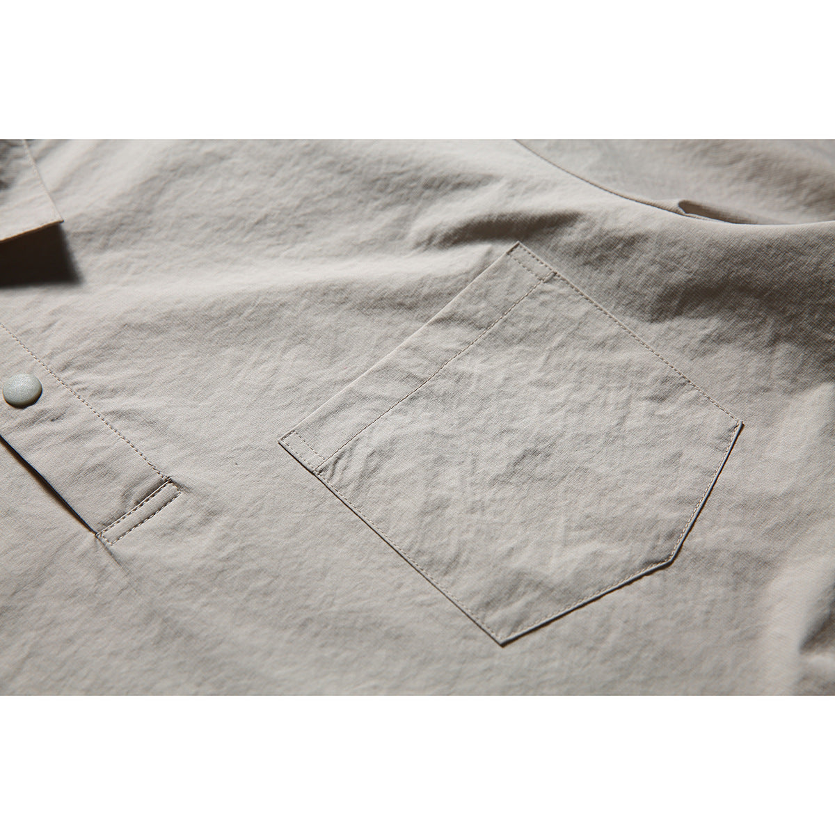 Close-up of the taupe shirt's stitched chest pocket, fabric texture and snap placket.