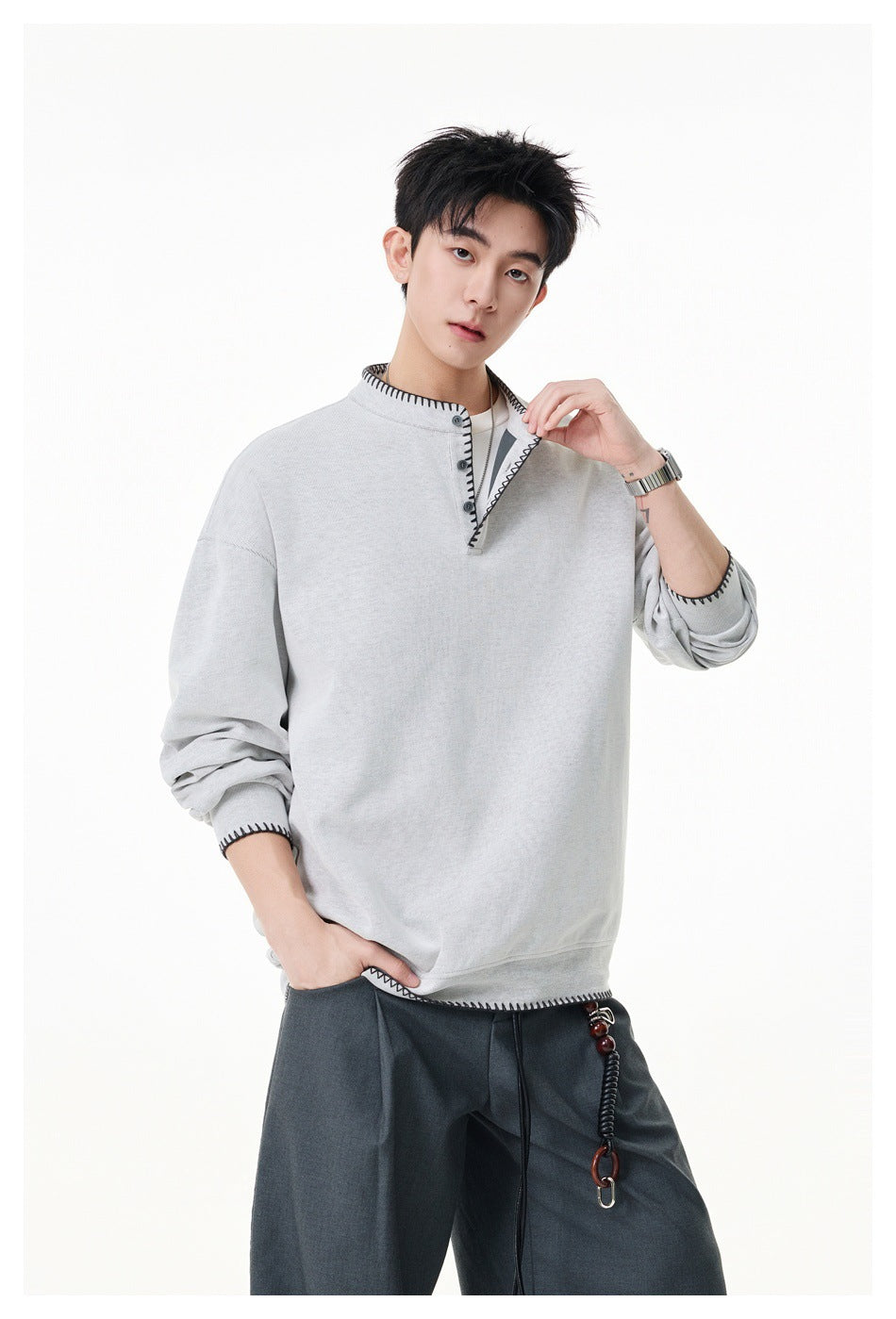 Model wearing a light gray oversized pullover with black contrast stitching and a short button placket.