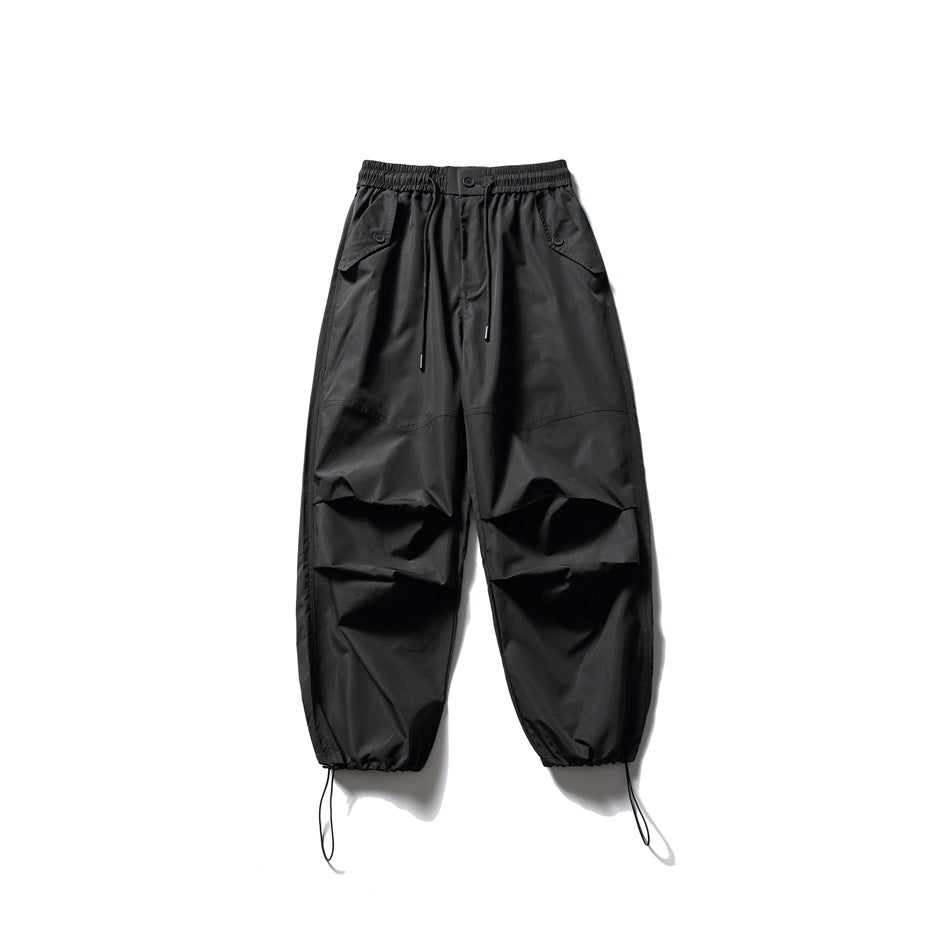 Front view of black wide-leg utility pants with an elastic drawstring waist, flap pockets, knee pleats, and ankle cords.