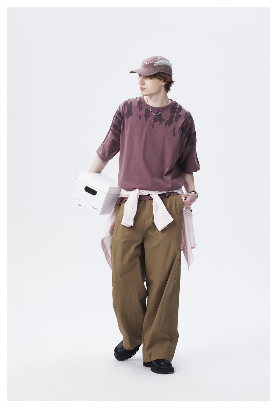Model wearing a mauve oversized graphic T-shirt, olive wide-leg cargo pants, and a pale pink shirt tied at the waist.