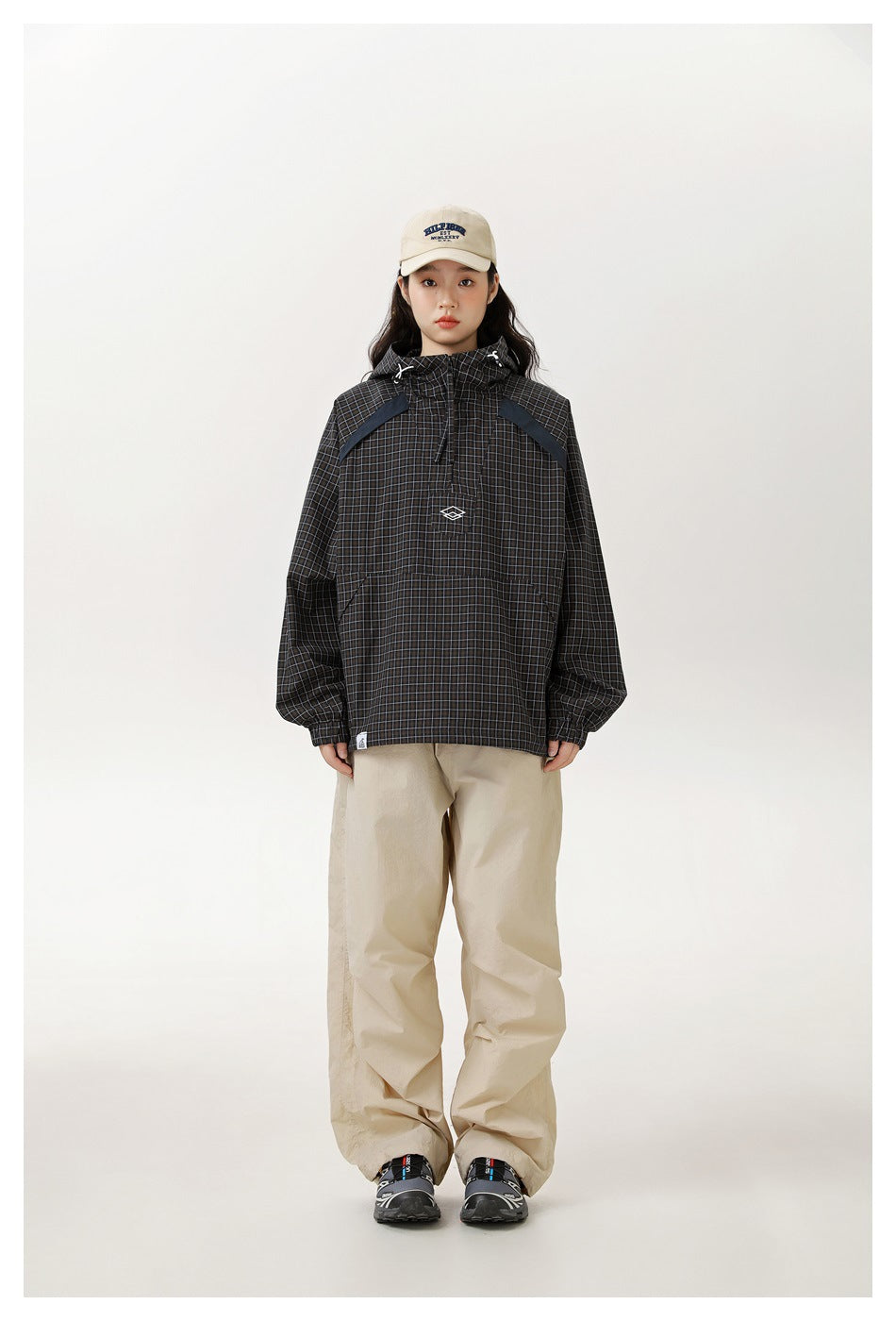 Model wearing the grid check hooded half-zip jacket with beige wide-leg pants, a cream cap and sneakers, full-length view