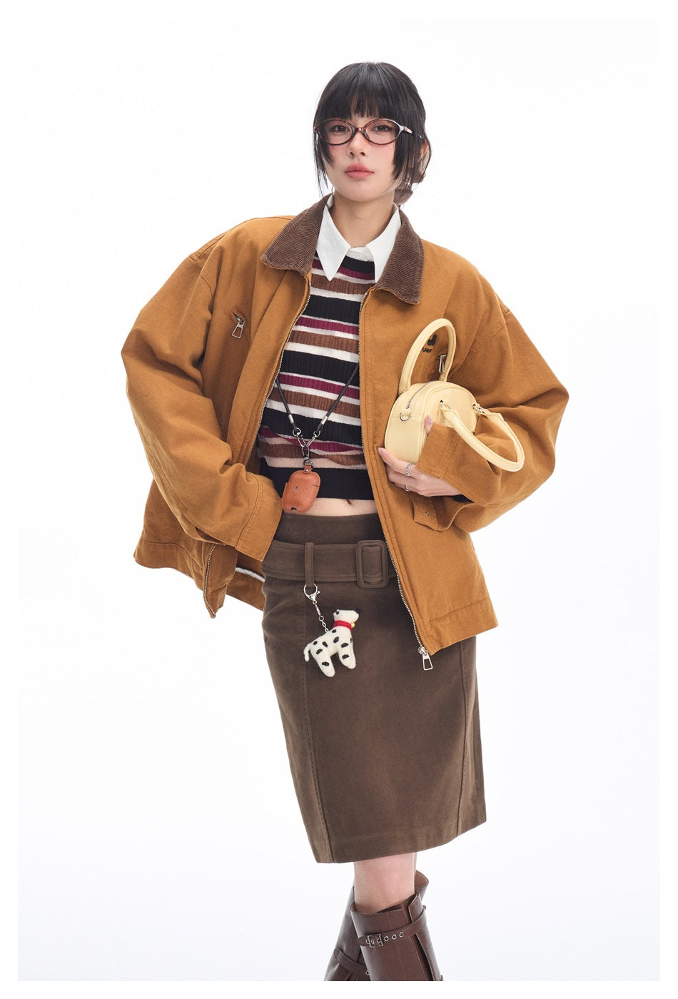 Model wearing the open tan-brown jacket with brown collar over a striped top, holding a small cream bag, three-quarter view