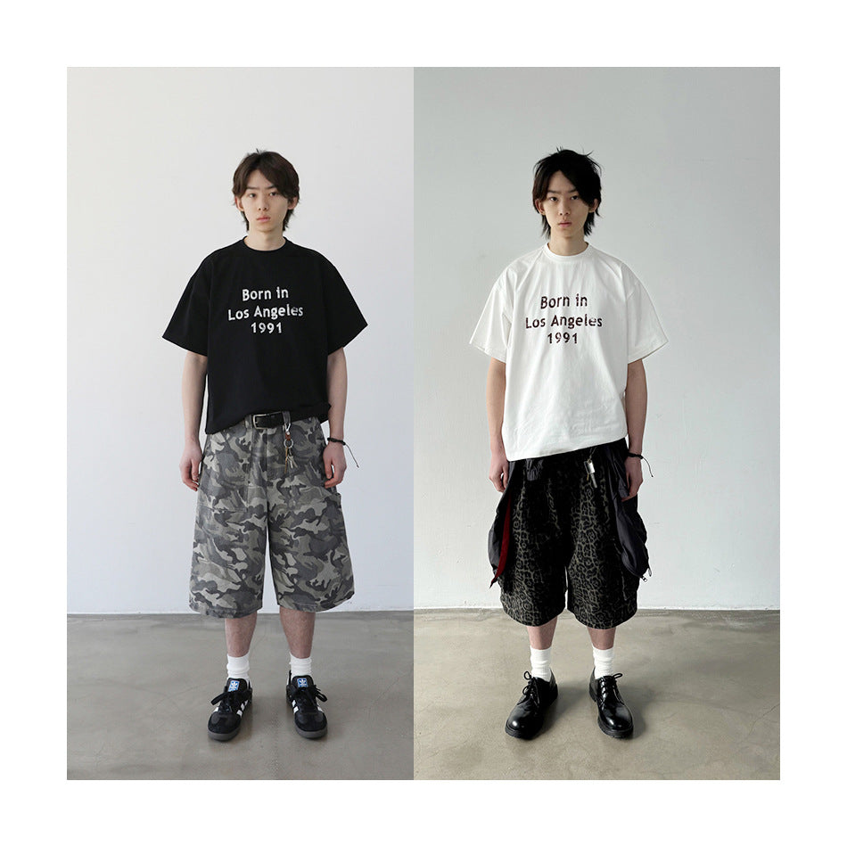 Two models wearing black and off-white 'Born in Los Angeles 1991' T-shirts with camouflage and leopard-print shorts