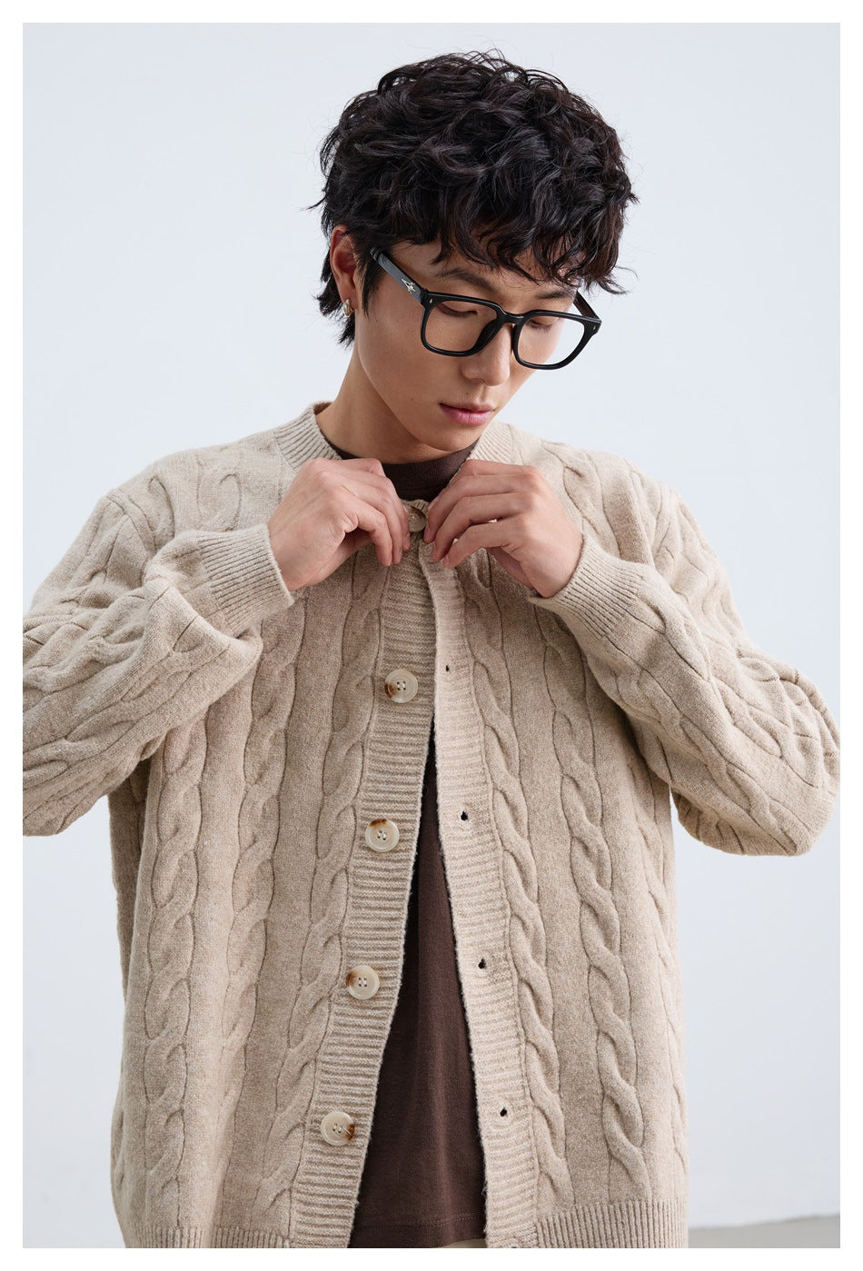Close front view of a person wearing a beige cable-knit cardigan with large buttons and ribbed trim.