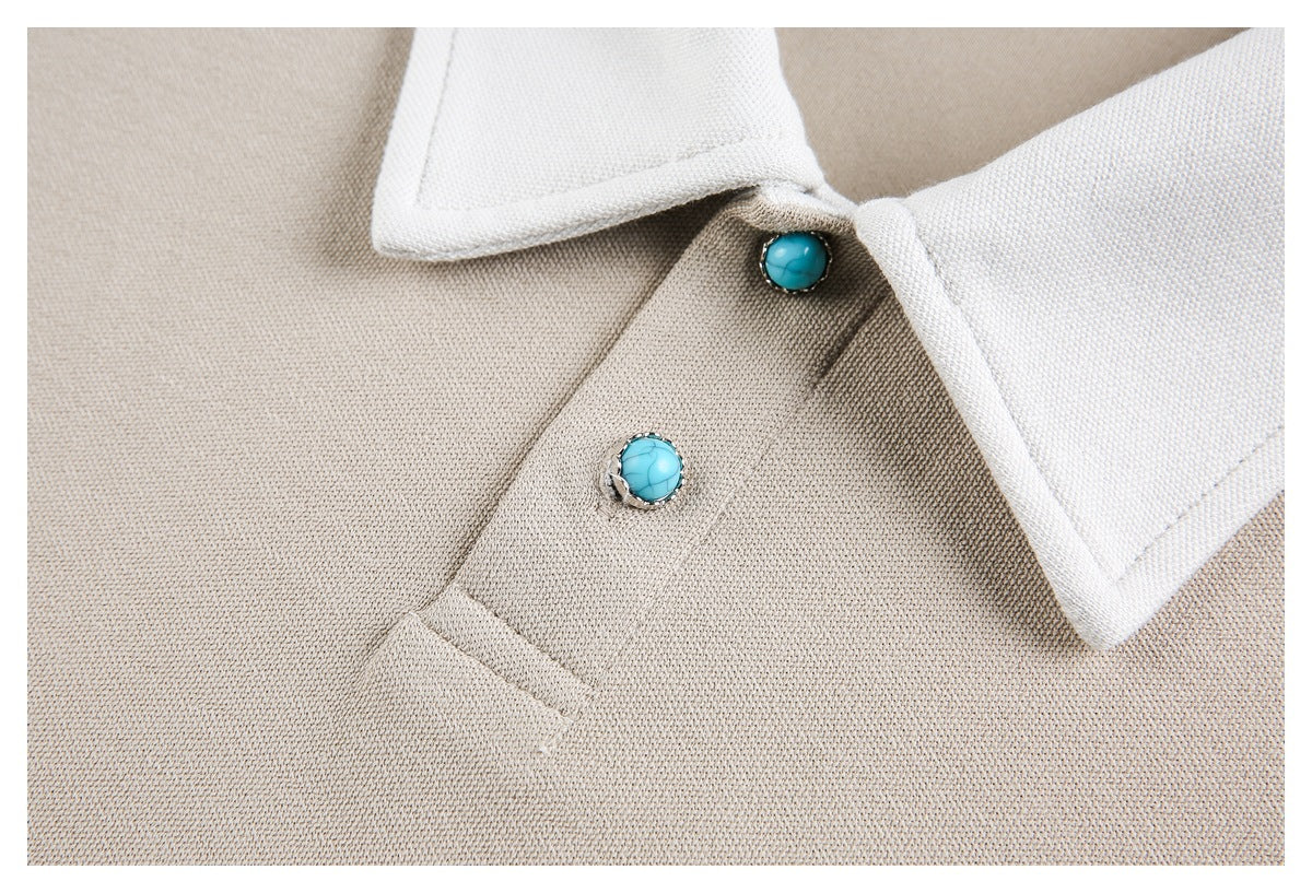 Close-up of a beige garment's white collar, placket, and two turquoise buttons.