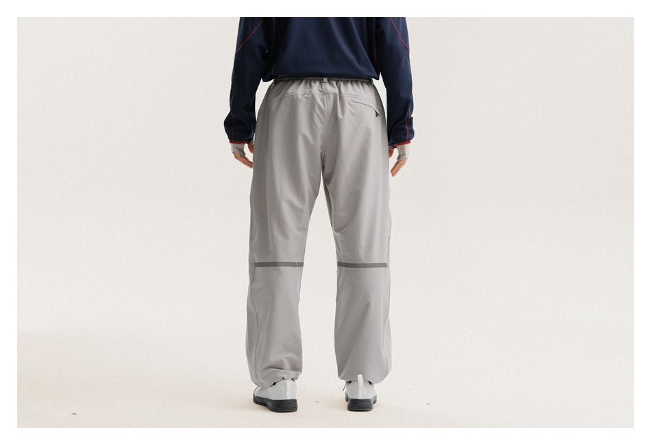 Rear view of a cropped model wearing loose light-gray pants with an elastic waist and dark bands around the lower legs.