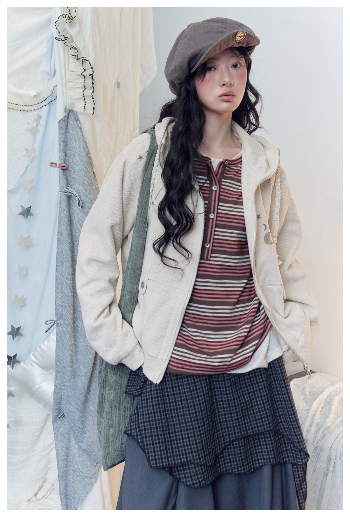 Closer view of a model in an ivory zip hoodie with star and moon details, layered over a burgundy striped top.