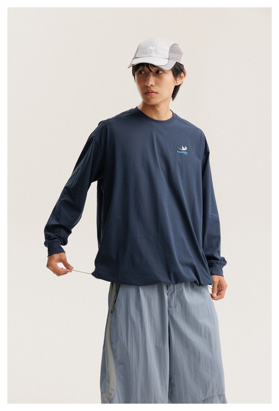 Model wearing a navy long-sleeve crewneck shirt with a small chest graphic and pale blue wide-leg pants.