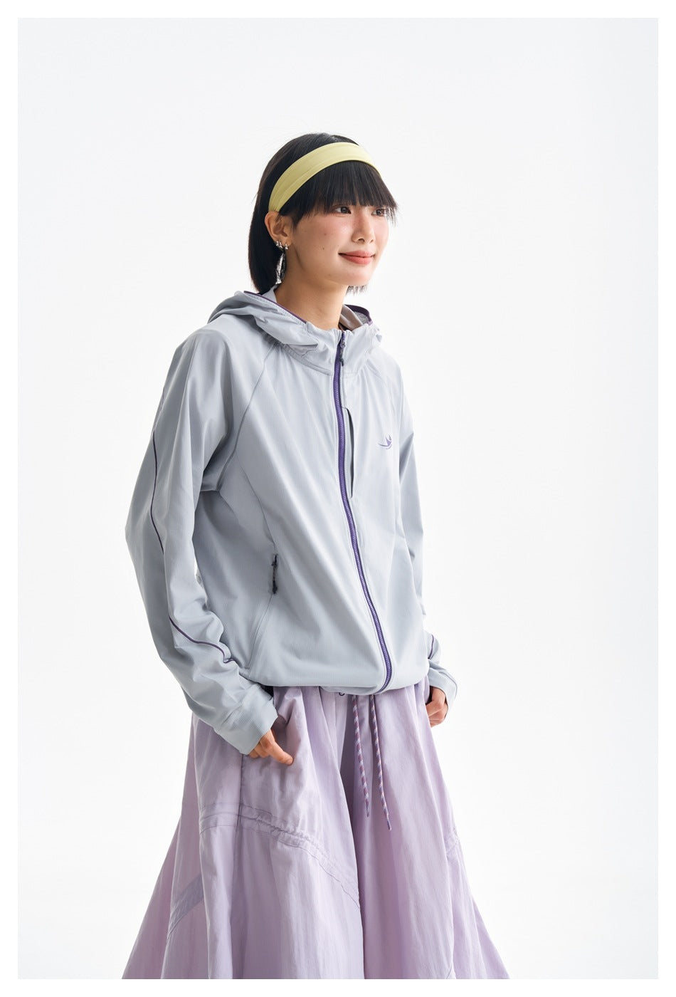 Closer front view of a model wearing a light gray hooded jacket with a purple zipper and lavender skirt.