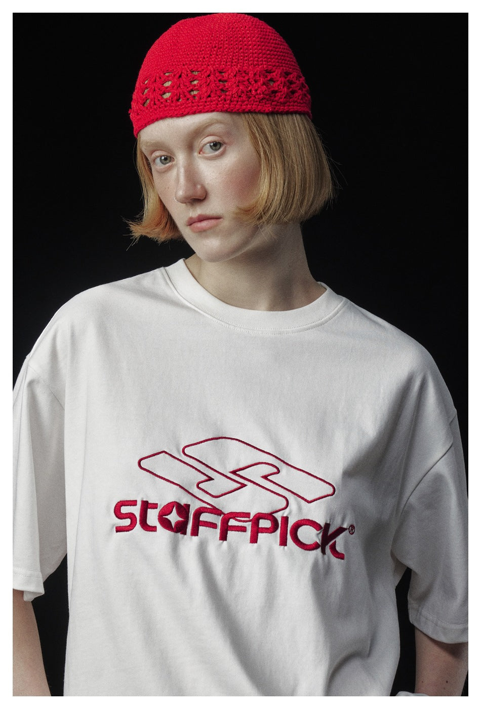 Close view of a model wearing a white T-shirt with red chest lettering and a red knit cap.