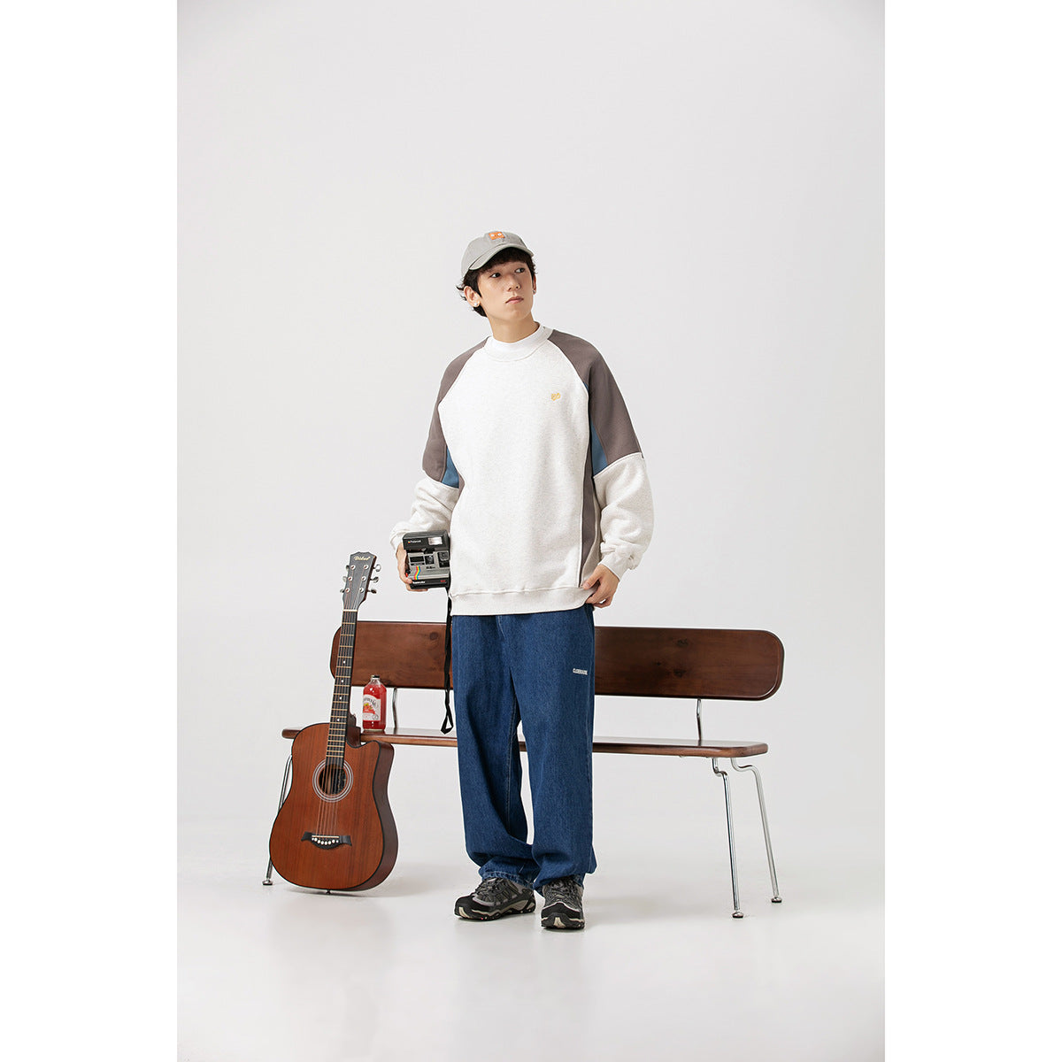 Model wearing an off-white color-block raglan sweatshirt with gray and blue panels, loose blue jeans, and a gray cap.