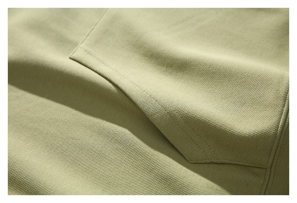 Close-up showing the muted olive hoodie’s kangaroo pocket seam and textured knit surface.
