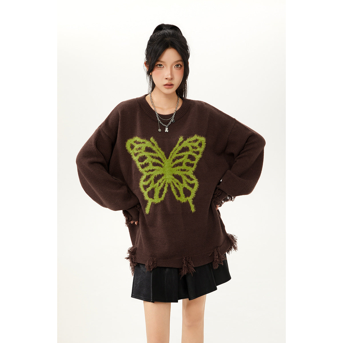 Model wearing an oversized dark brown sweater with a lime-green butterfly and tasseled hem, paired with a black skirt.