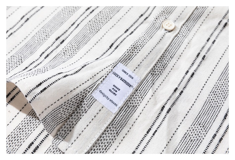 Close-up of a sewn-in label on the cream shirt, surrounded by its black stripe pattern and a white button.