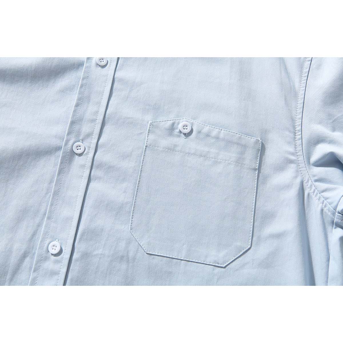 Close-up of a pale blue shirt front pocket with a button and nearby placket.