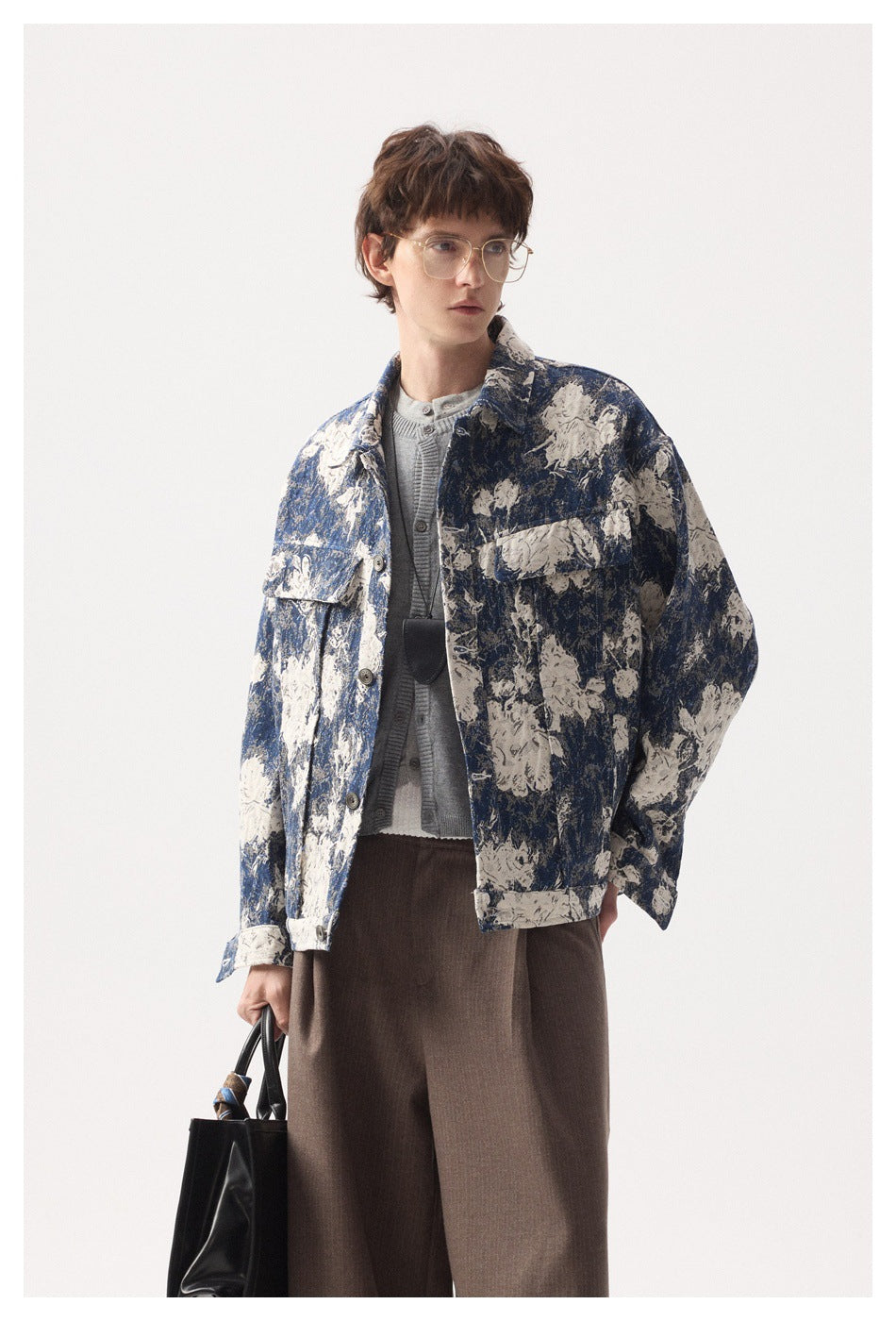 Model wearing a blue and cream floral button jacket over gray knitwear, shown from the front with a black bag.