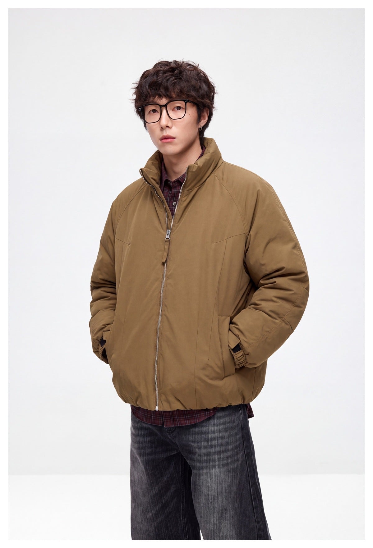 Man wearing tan brown zip-front padded jacket with stand collar over plaid shirt, hands in pockets