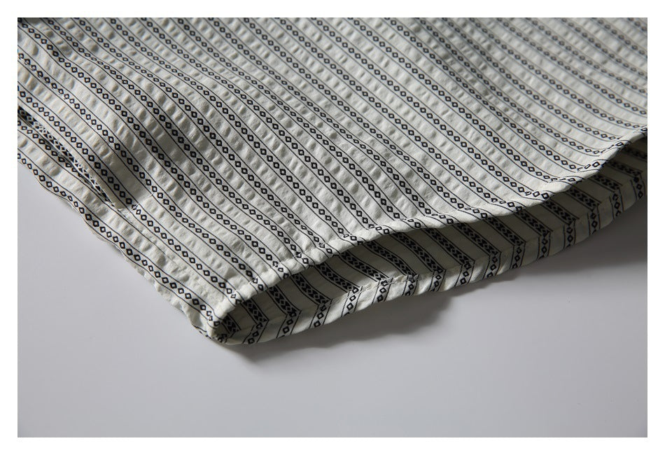 Close-up of the folded hem of a cream shirt with repeating black geometric stripes.
