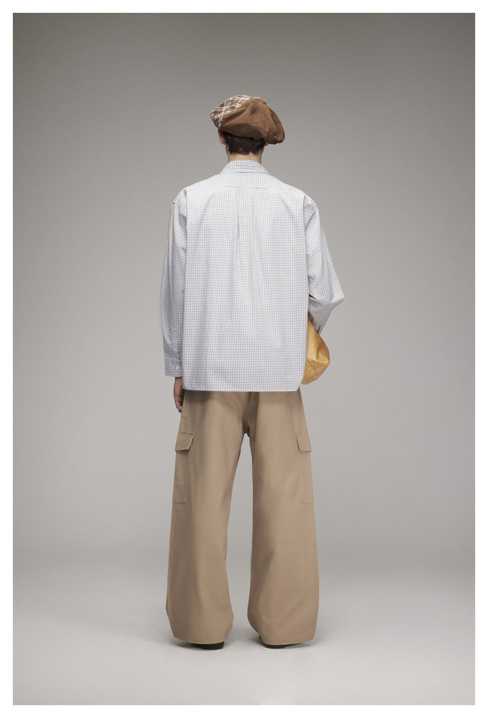 Rear view of a model in a light gray checked shirt and wide-leg tan cargo trousers.
