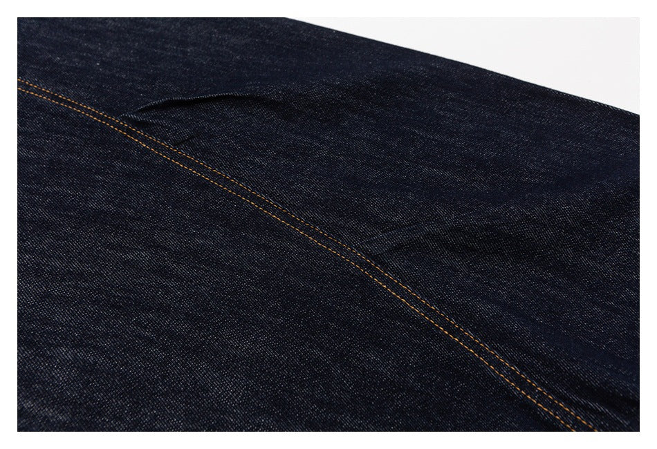 Close-up of dark indigo denim with a curved seam and contrasting golden-orange stitching.