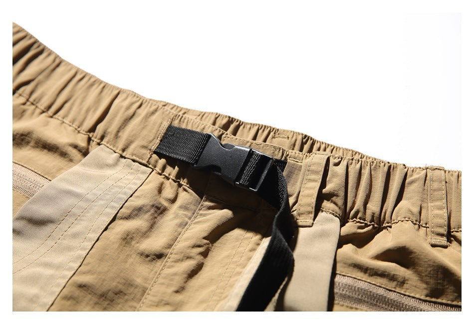 Close-up of the gathered waistband and adjustable black buckle belt on tan utility shorts.