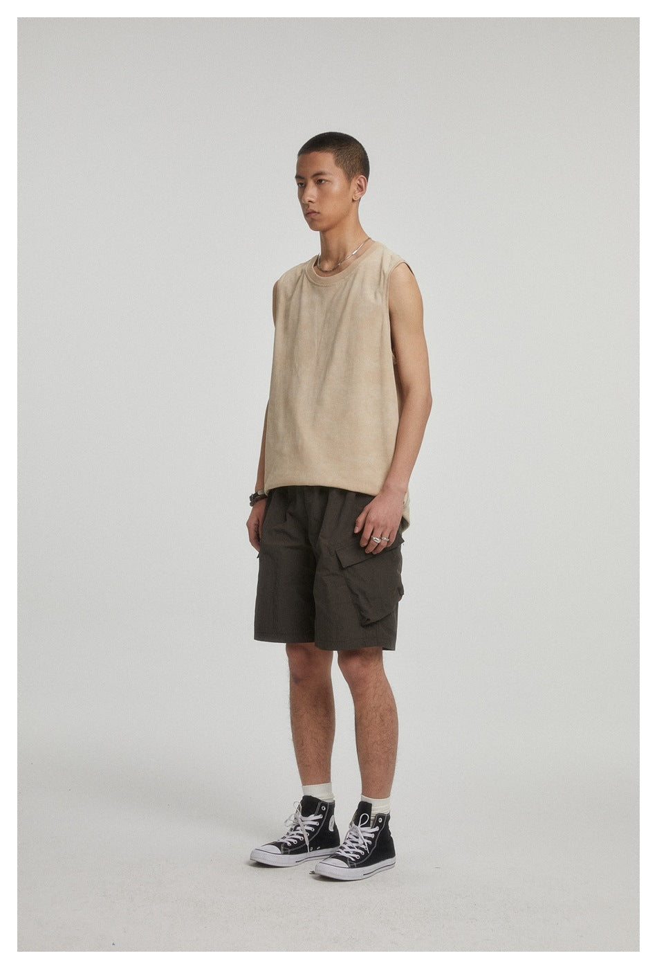 Three-quarter view of a man wearing a beige sleeveless top and dark cargo shorts.