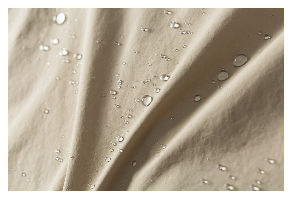 Water droplets bead on folded light tan garment fabric.