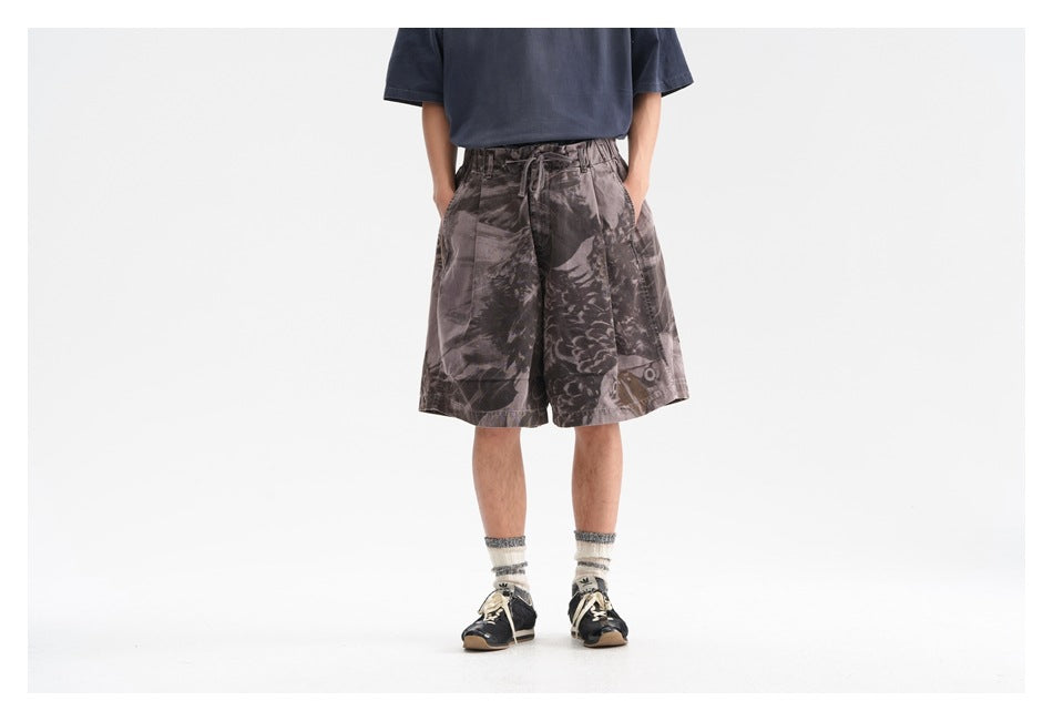 Person wearing wide-leg gray-brown printed shorts with drawstring waist, navy tee, white socks and dark sneakers