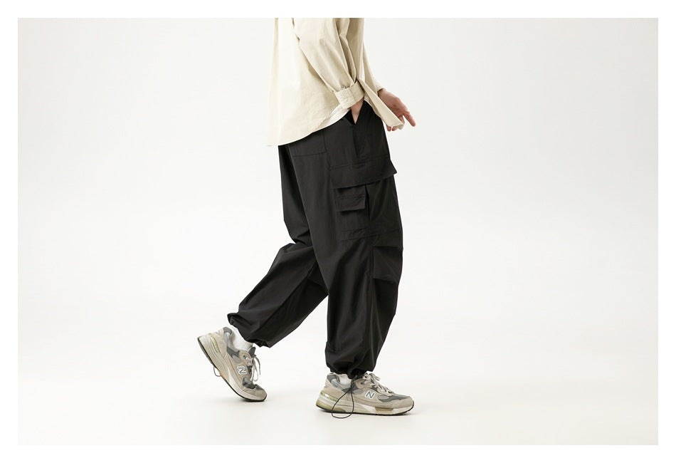 Side view of a model wearing black cargo pants with multiple flap pockets and elasticated ankles.