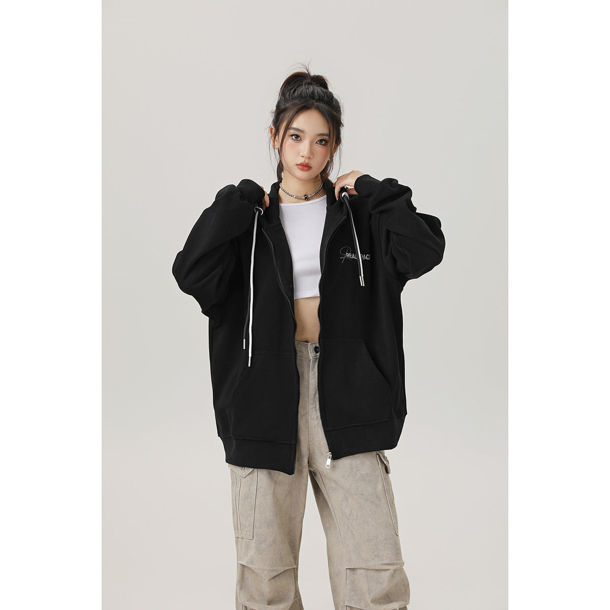 Front view of a model in an oversized black zip-up hoodie with white drawstrings, worn open over a white top.