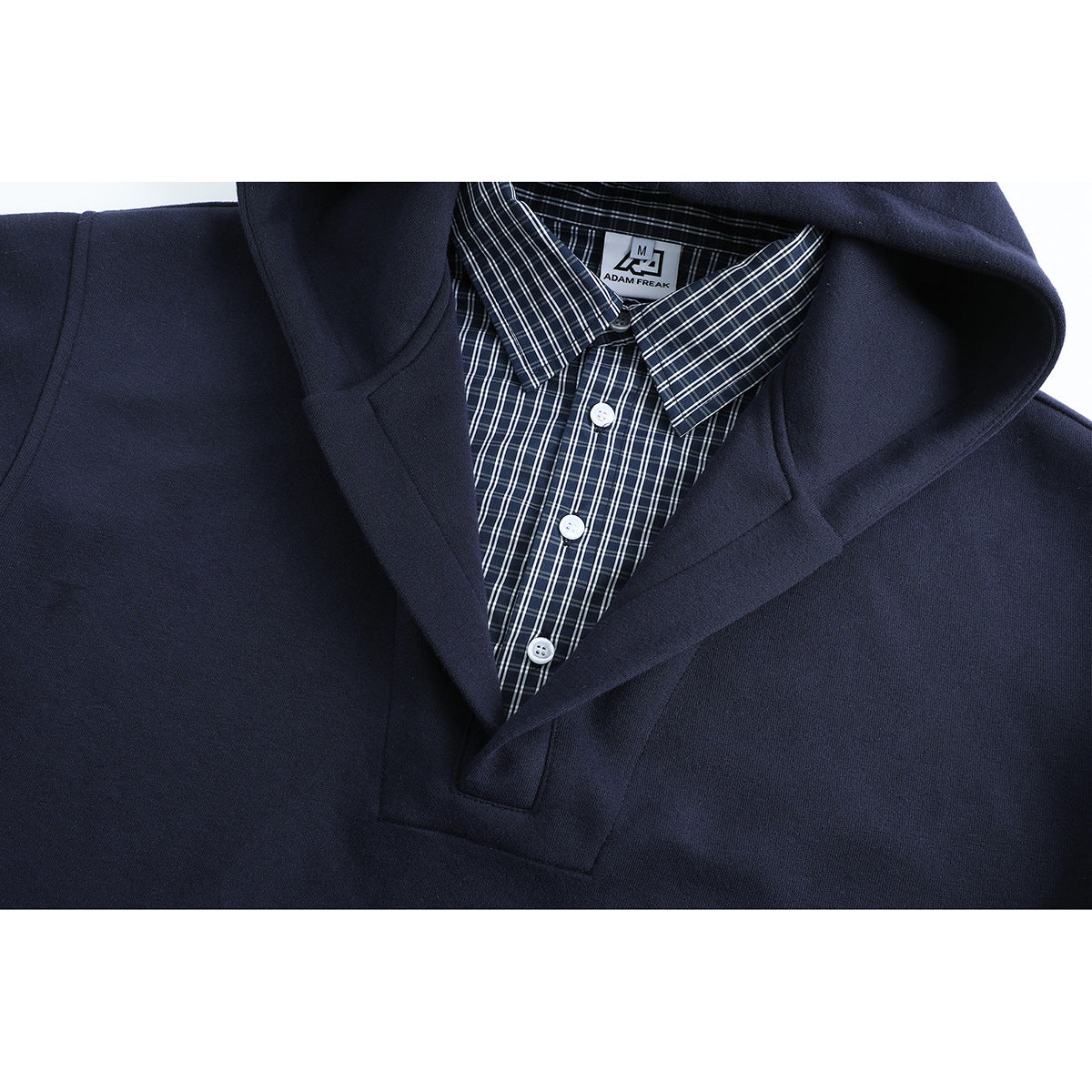 Close-up of a navy hooded pullover layered over a dark plaid button-up shirt, showing the collar and placket.