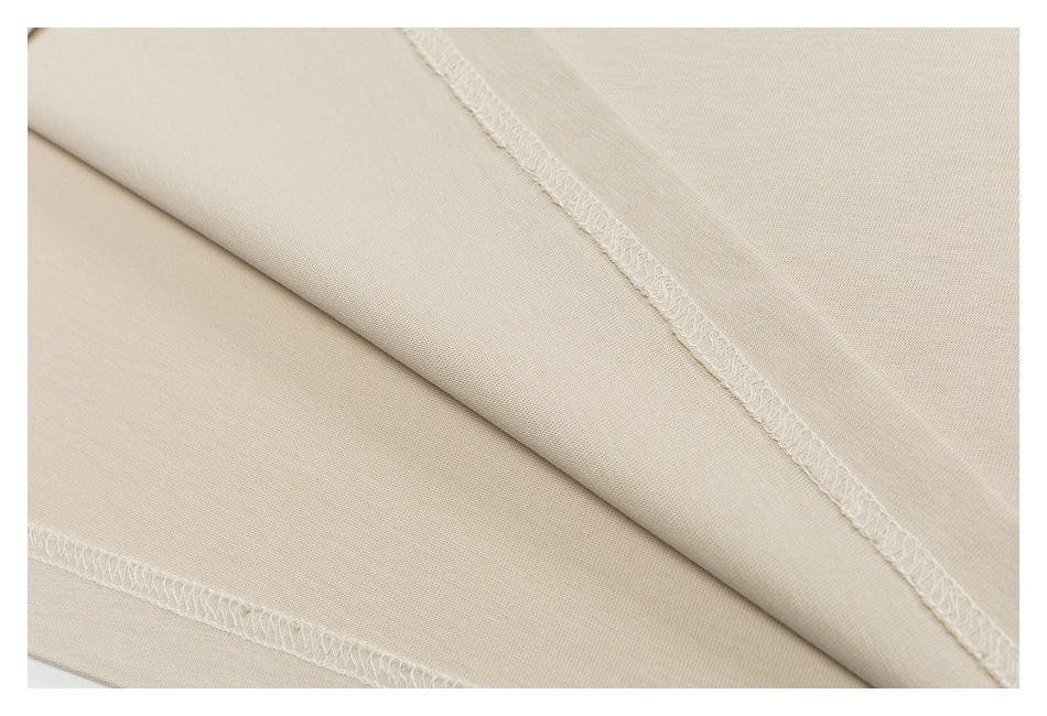 Close-up of beige T-shirt fabric and intersecting seams with overlocked stitching.