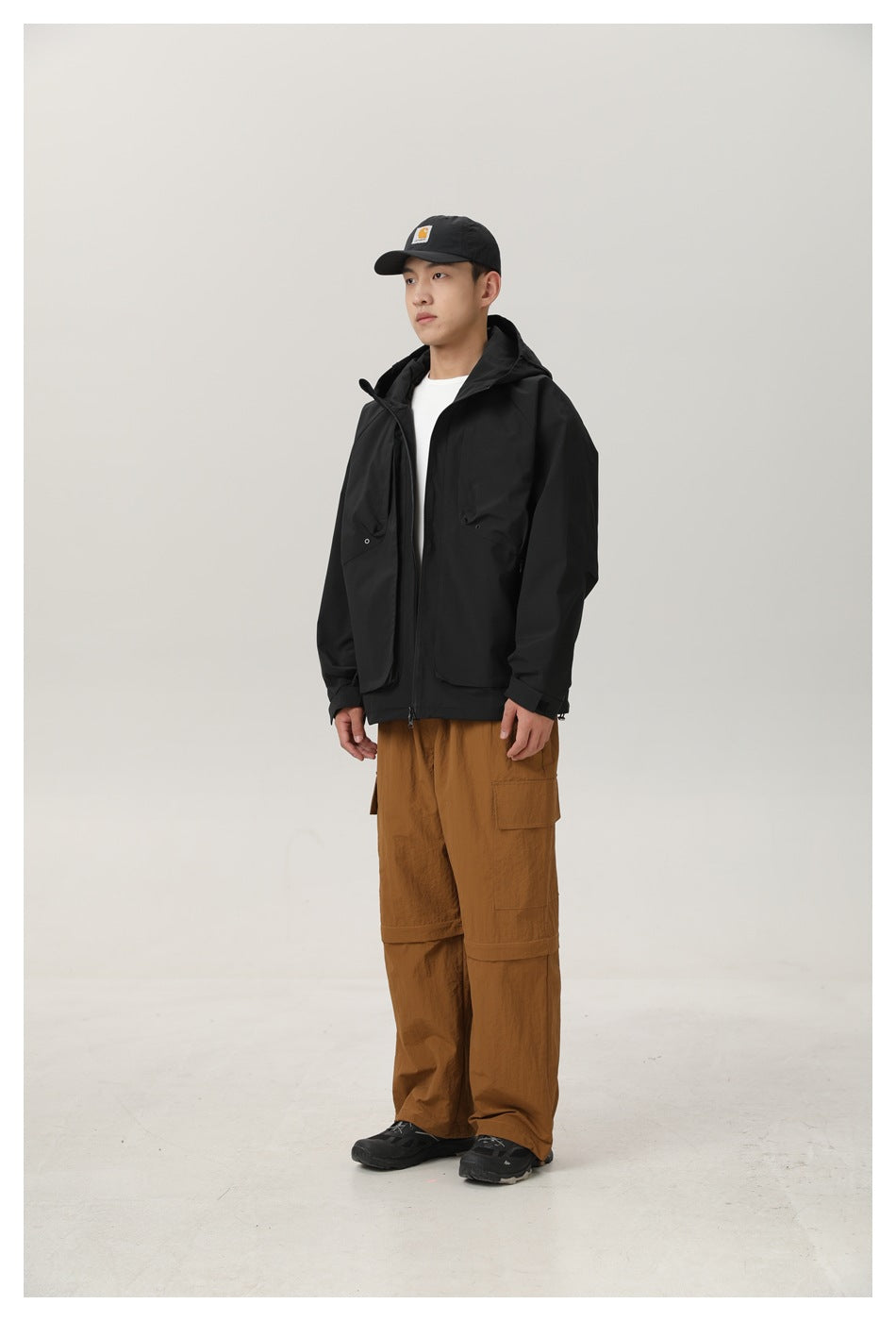 Model wearing a black hooded zip jacket over a white tee with brown cargo pants, angled side view