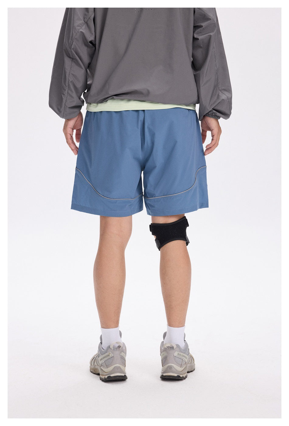 Rear view of a person wearing blue athletic shorts with curved contrast piping and a wide hem.