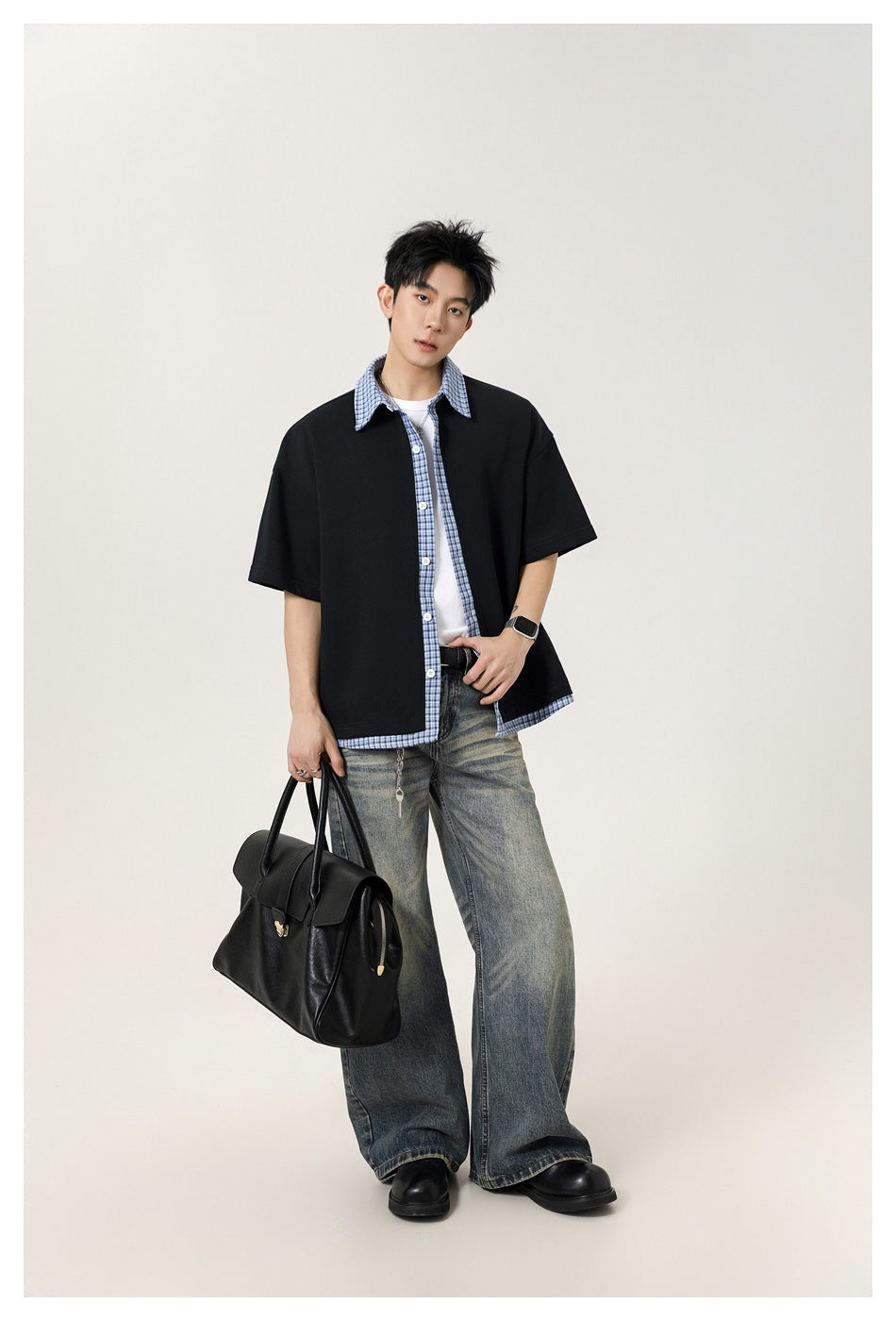 Full-length view of a model wearing a black short-sleeve shirt with blue plaid trim and wide faded jeans.