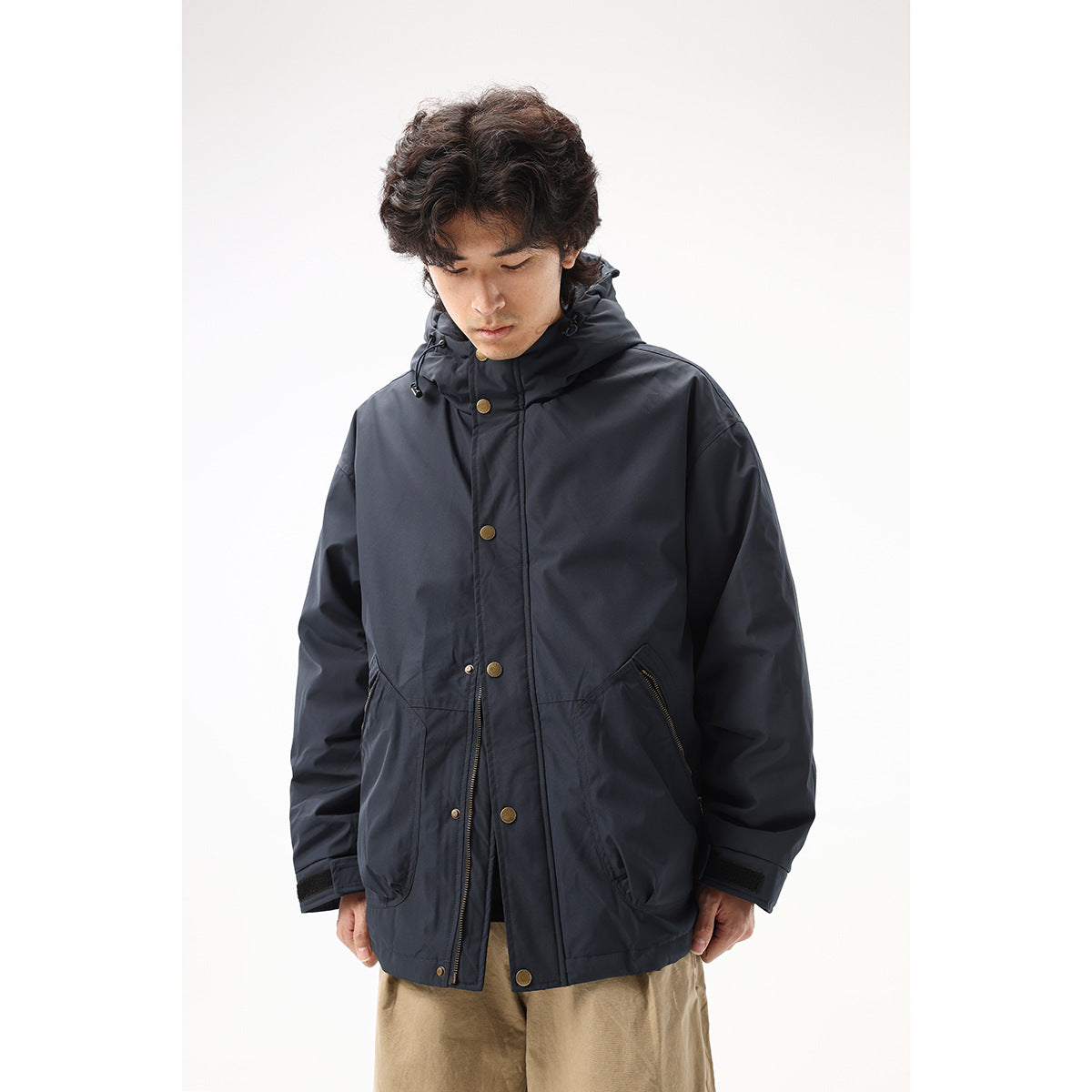 Close front view of a model wearing a dark navy hooded jacket with brass-tone snaps and zippered pockets.