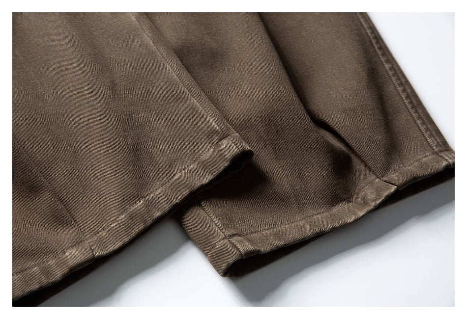 Close-up of brown trouser legs and stitched hems against a white background.