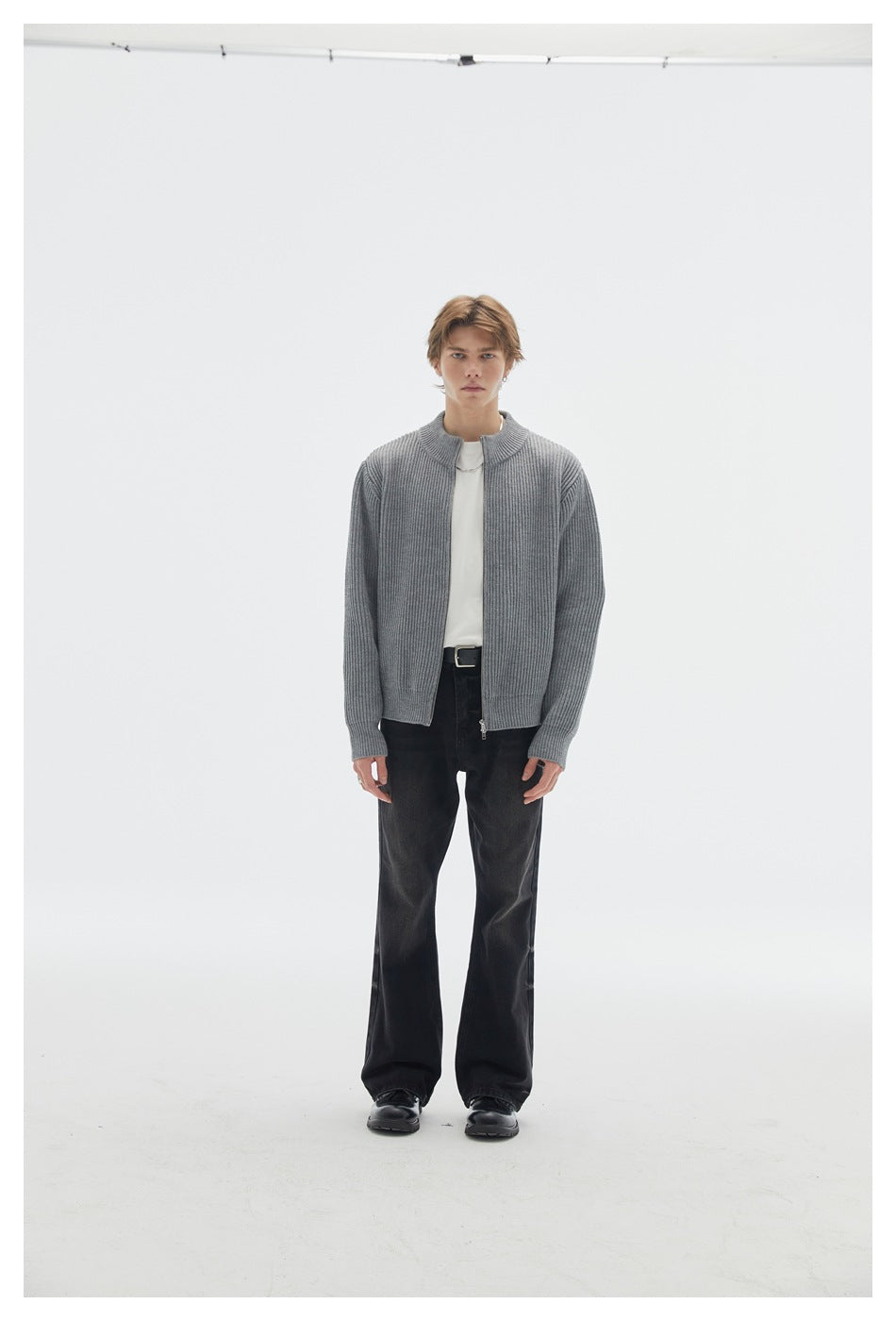 Full-length front view of a model wearing a gray ribbed zip cardigan, white shirt, and black trousers.