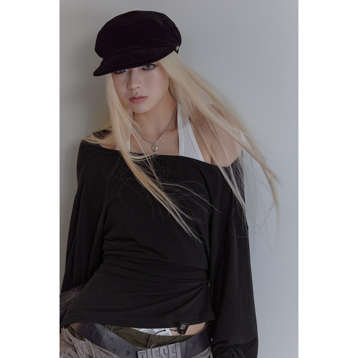 Model wearing a black off-shoulder long-sleeve top over a white halter top, with a black cap.