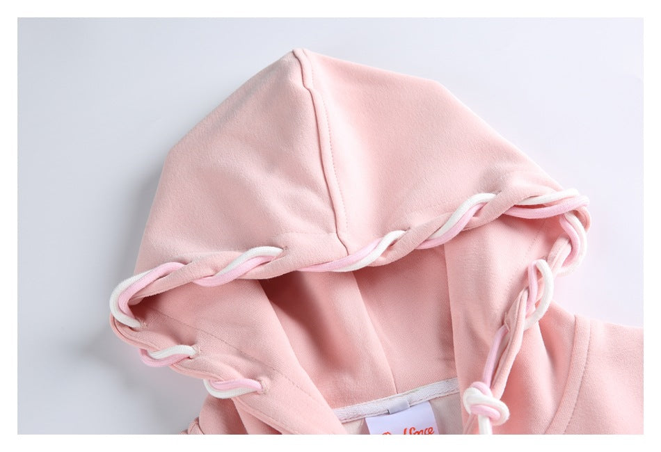Close-up of a pale pink hoodie showing the hood seam and white-and-pink cords threaded around its edge.