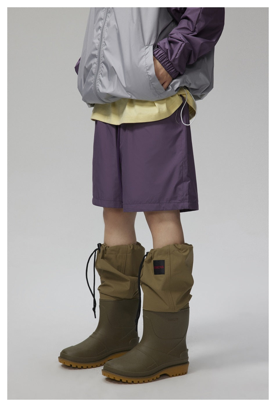Cropped view of a person wearing a gray and purple jacket, purple shorts, and olive knee-high boots with gathered cuffs.