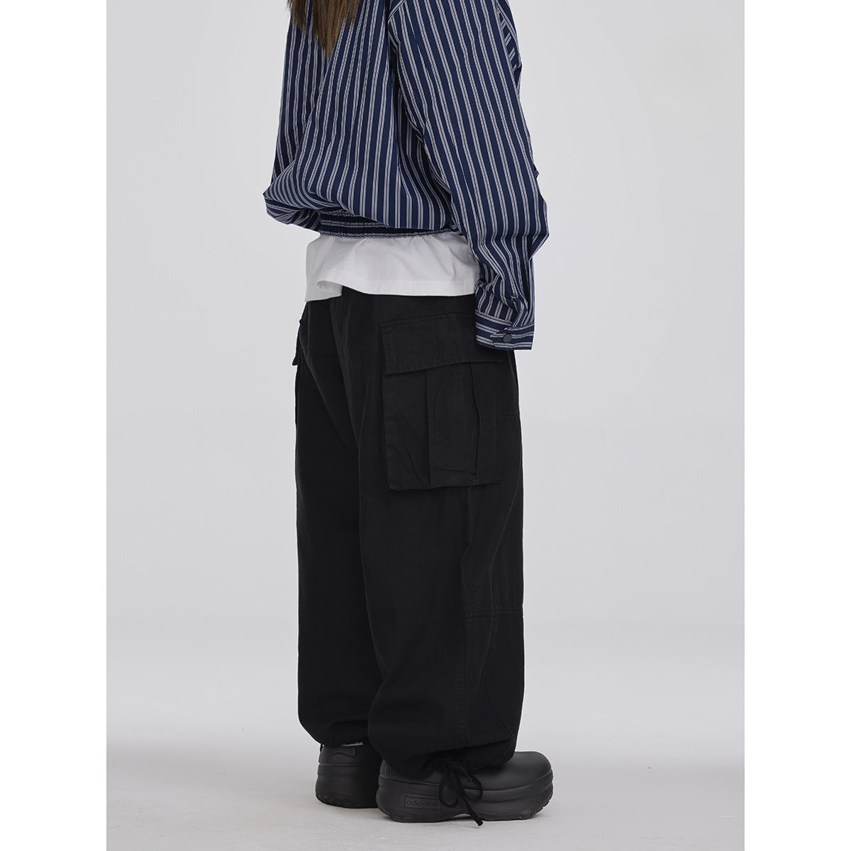 Side view of a model wearing loose black cargo pants with a large flap pocket and drawstring ankle cuffs.